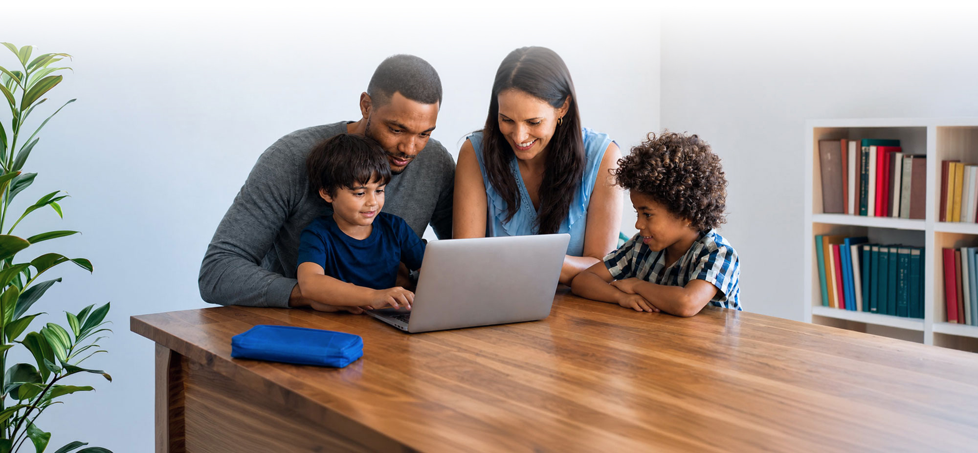 A father, mother, and their two sons look at a laptop together at home.