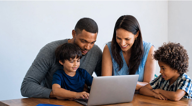 A family gathers around a laptop together at home.